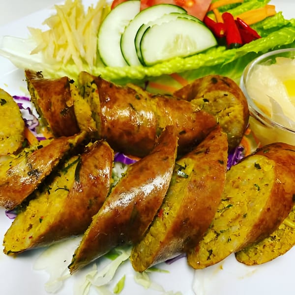 Sliced Thai sausage with a vibrant yellow filling, served with fresh vegetables and a dipping sauce.