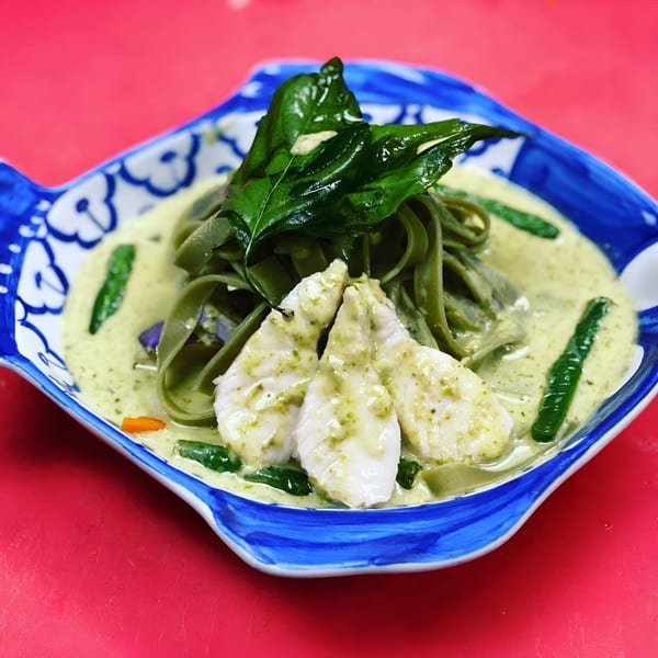 Thai green curry with fish fillets, green noodles, and basil in a fish-shaped bowl.
